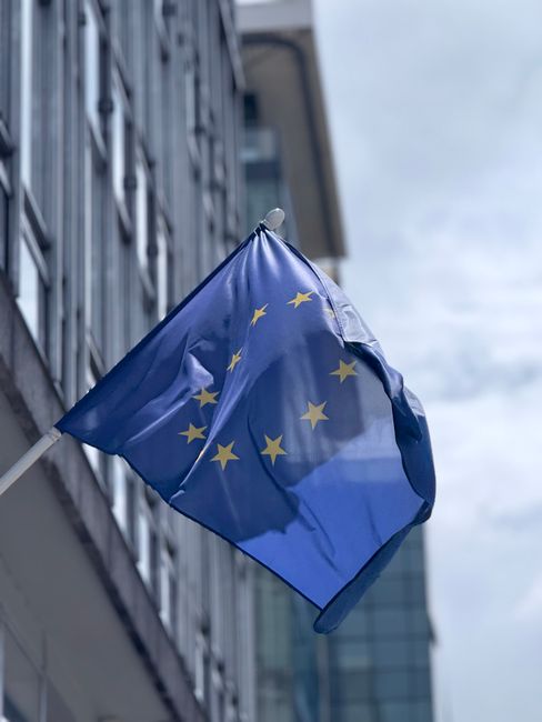 EU-flaggan vajar framför en modern glasbyggnad en molnig dag