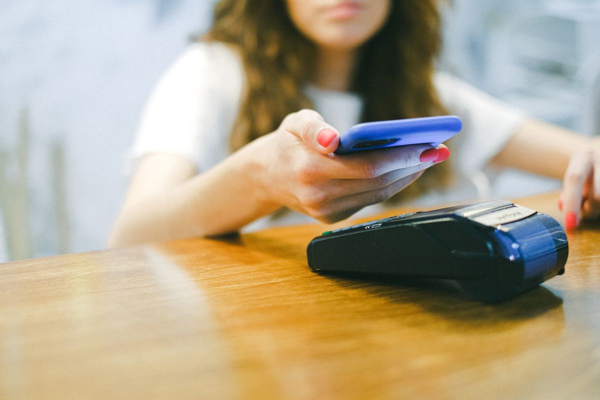Kvinna betalar kontaktlöst med sin smartphone vid en betalterminal