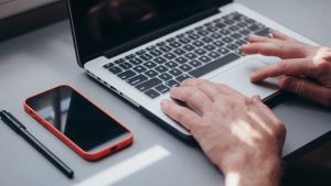 Hur tar man en skärmdump? Så gör du på Mac, Windows, iPhone och Android Händer som skriver på en laptop med en mobil bredvid – ta skärmdump på dator och telefon