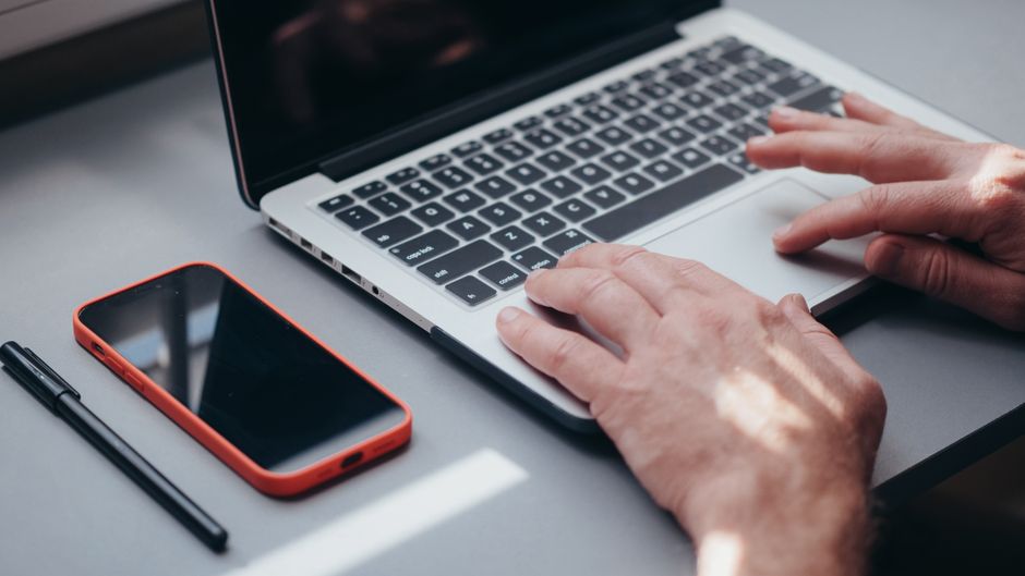 Händer som skriver på en laptop med en mobil bredvid – ta skärmdump på dator och telefon