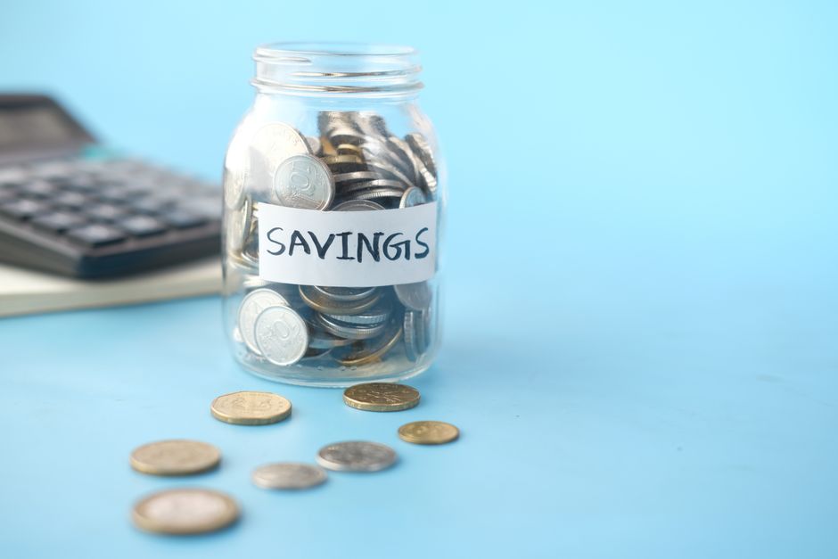 Glasburk märkt Savings fylld med mynt bredvid en miniräknare